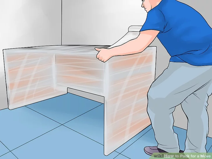 A man wrapping a wooden desk tightly in plastic stretch wrap before a move
